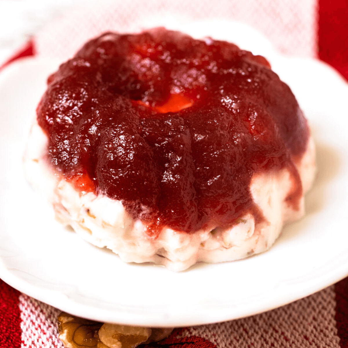 3/4 angled of a molded Frozen Cranberry Salad sitting on a white plate over a red striped towel.