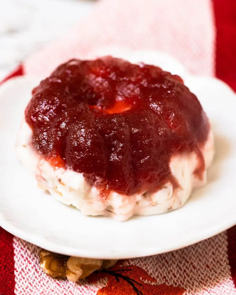 3/4 angled of a molded Frozen Cranberry Salad sitting on a white plate over a red striped towel.