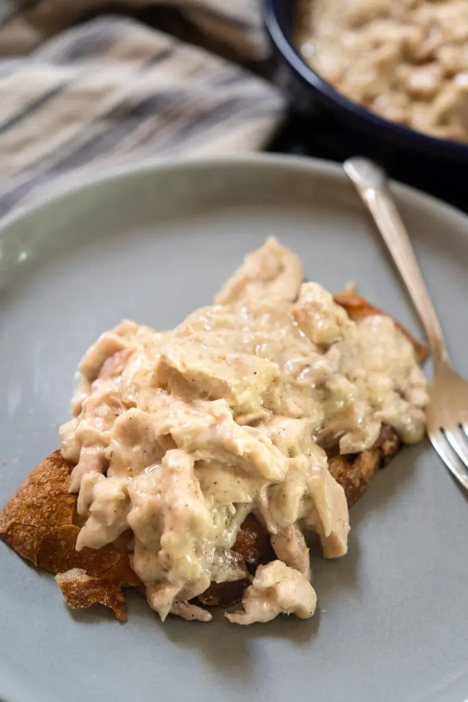 Top down photo of crusty bread topped with creamed turkey filling on a gray plate. A fork sits next to the sandwich. A bowl of the filling sits in the background.