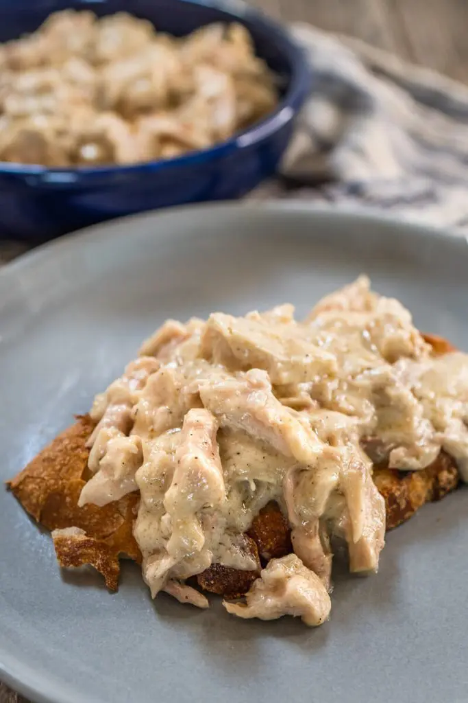 3/4 angle photo of crusty bread topped with creamed turkey filling on a gray plate. A fork sits next to the sandwich. A bowl of the filling sits in the background.