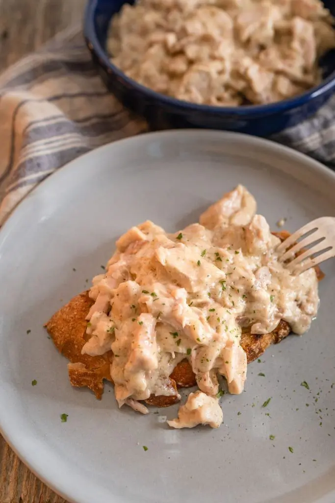 Top down photo of crusty bread topped with creamed turkey filling on a gray plate. A fork sits next to the sandwich. A bowl of the filling sits in the background.