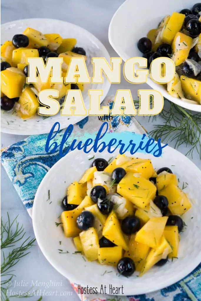 Top down view of cut up mangos and blueberries on a white plate garnished with fennel fronds.