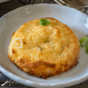 Top down close up potato cake garnished with sliced green onions sitting on a white plate.