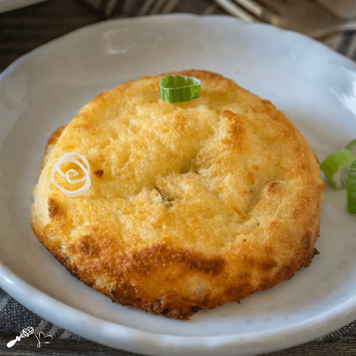 Top down close up potato cake garnished with sliced green onions sitting on a white plate.