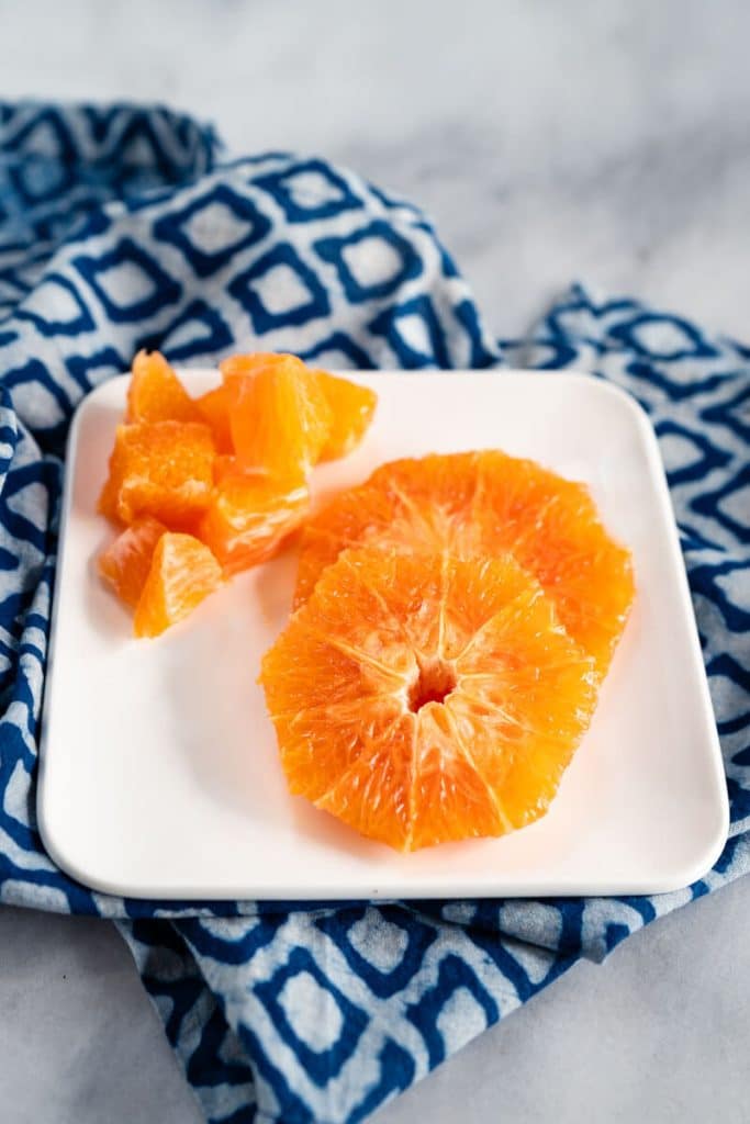 Top-down shot of a sliced orange and diced orange pieces sitting on a white plate.