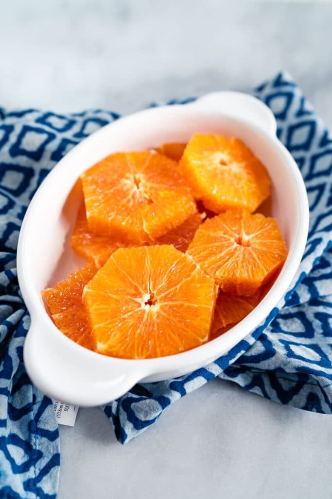 White oval dish filled with slices of fresh orange over a blue checked napkin.