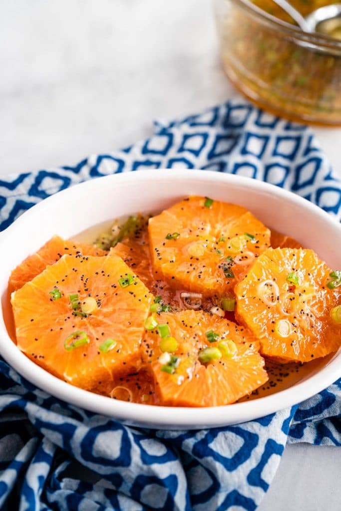 White dish filled with sliced oranges drizzled with a poppyseed vinaigrette and garnished with feta, walnuts, and sliced green onions.