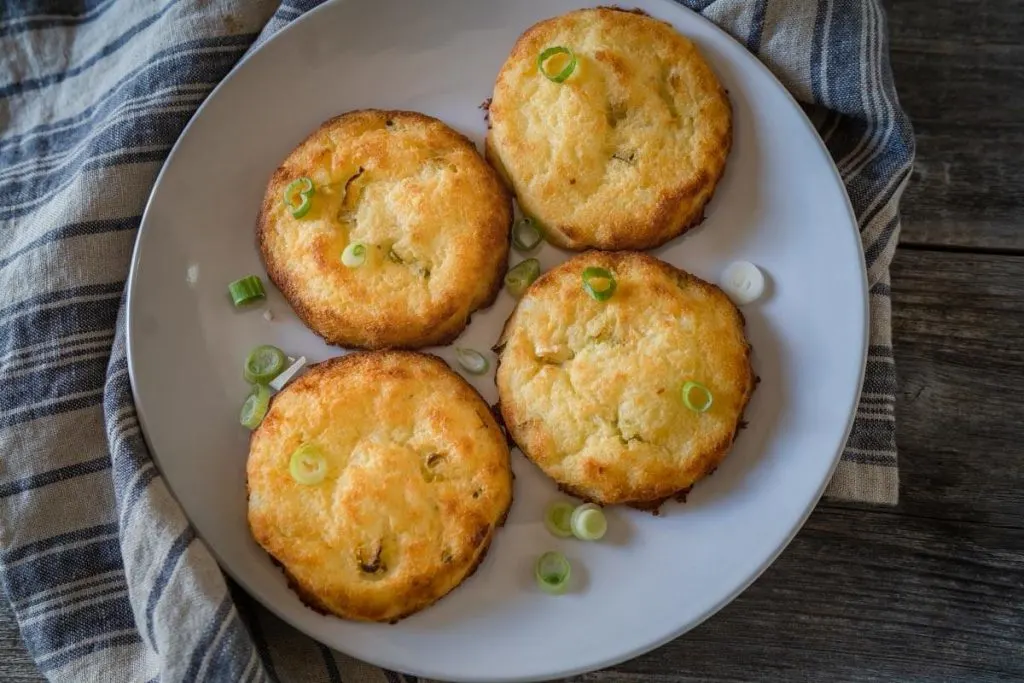 Top down photo of a gray plate holding baked potato cakes garnished with sliced green onions.