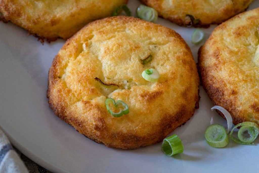 Top down close up potato cake garnished with sliced green onions sitting on a white plate.