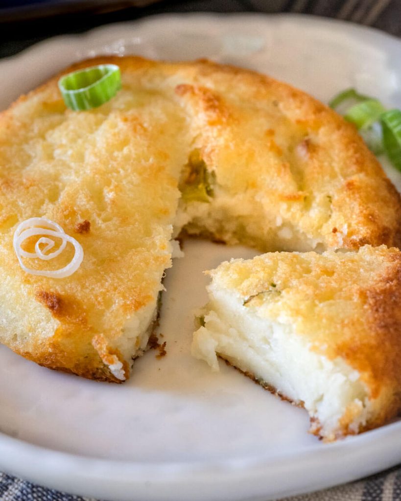 A sliced Potato Cake garnished with sliced green onions on a white.