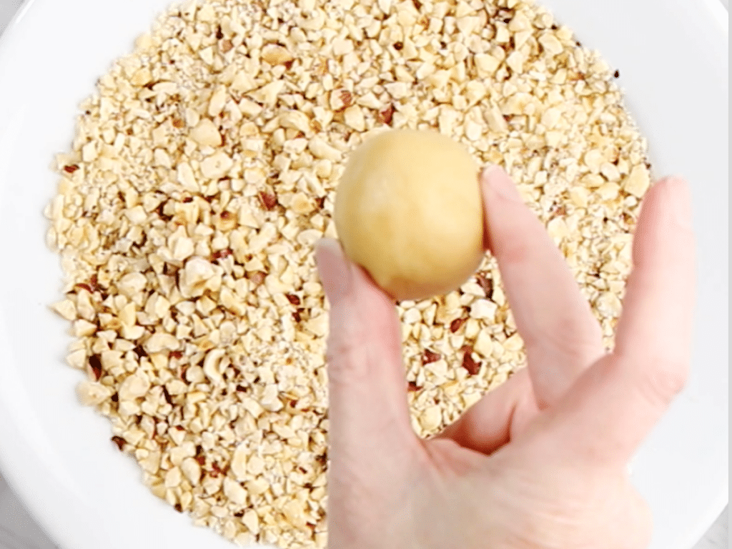 Shaped thumbprint dough hovering oven a bowl of chopped nuts.