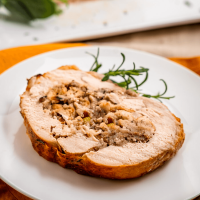 angled photo of a slice of turkey roulade stuffed with a swirl of stuffing on a white plate next to a rosemary garnish.