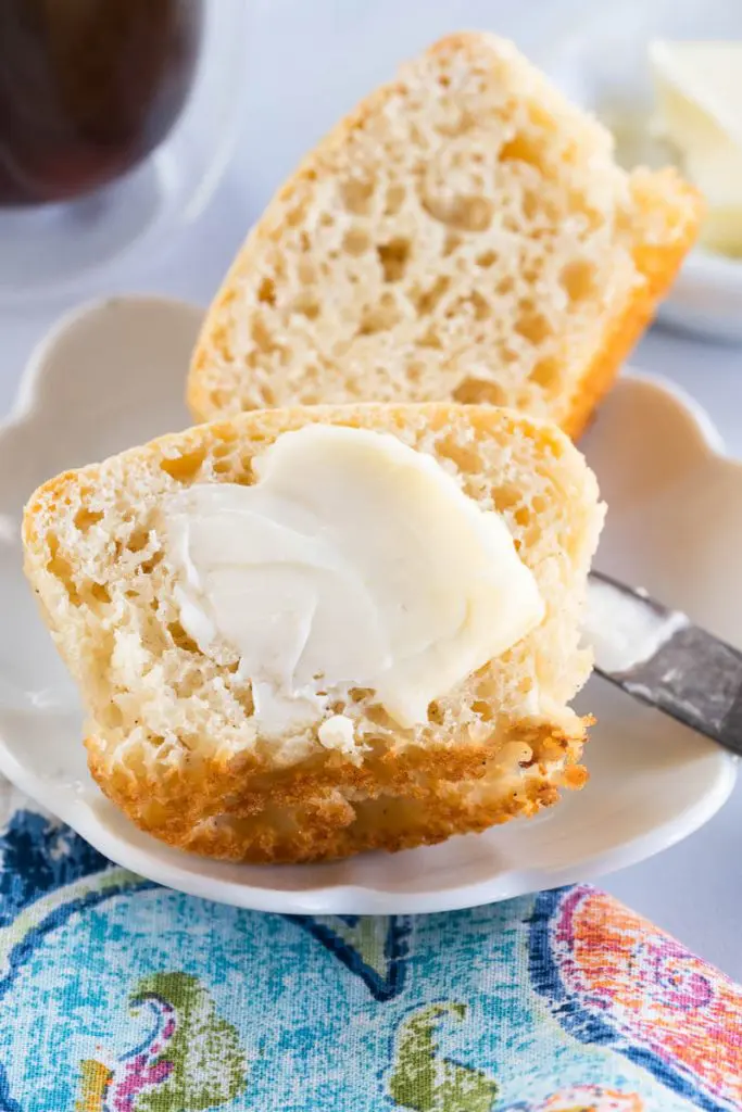 Close up of a vanilla muffin cut in half and slathered with butter.