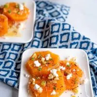 Top-down shot of two plates of fresh orange slices drizzled in a poppyseed vinaigrette and garnished with feta, sliced green onions, feta, and chopped walnuts.