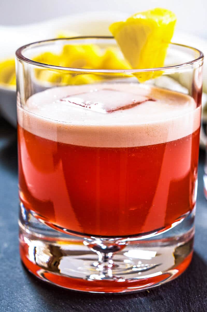 Sideview of a rock glass filled with a Campari Cocktail garnished with a piece of pineapple.