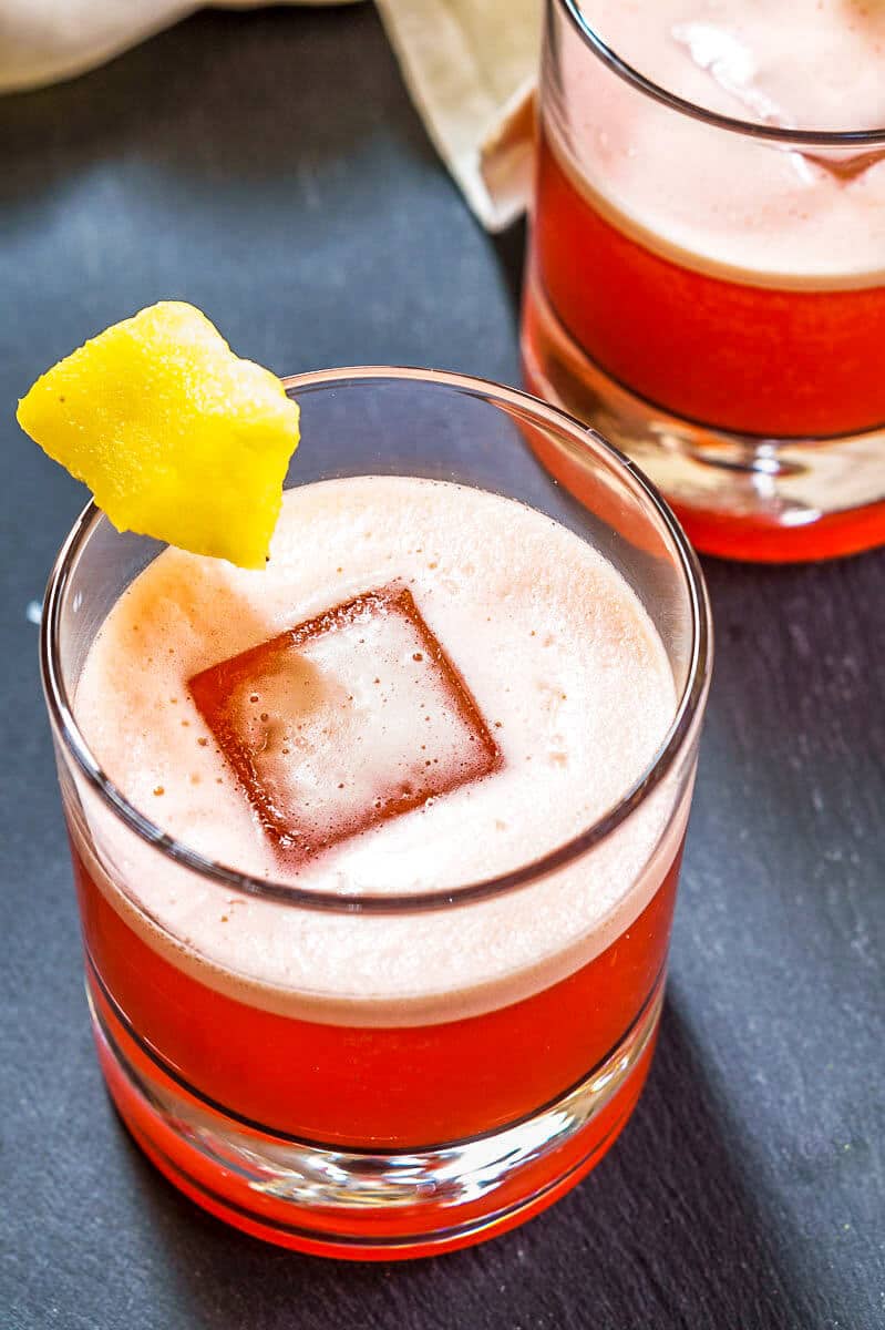 Top down view of a rocks glass filled with a red foam-topped Campari Cocktail garnished with a piece of pineapple.