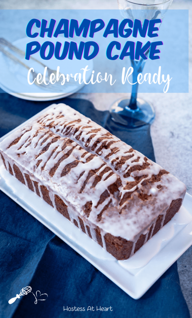 Top down view of a loaf of Champagne cake covered with a champagne drizzle sitting on a white platter over a blue napkin. A set of plates and a champagne glass sit int he background.