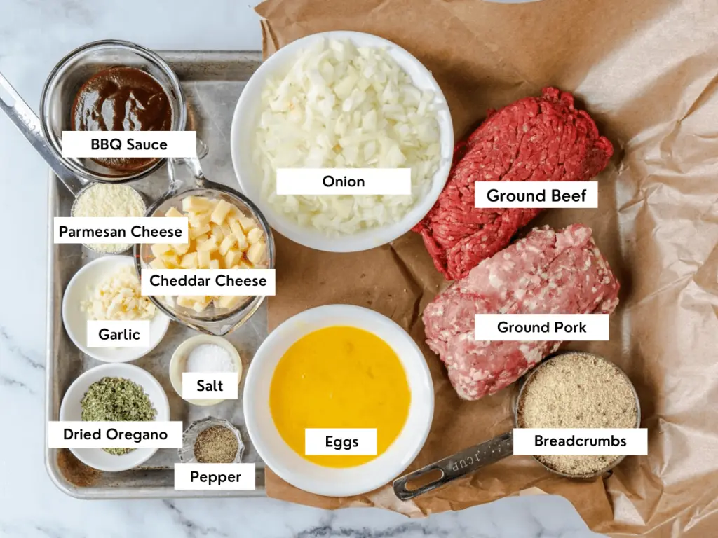 Top down view of the ingredients used in a cheese stuffed meatloaf including ground pork, ground beef, breadcrumbs, eggs, dried oregano, salt, pepper, garlic, cheddar cheese, onion, and garlic.