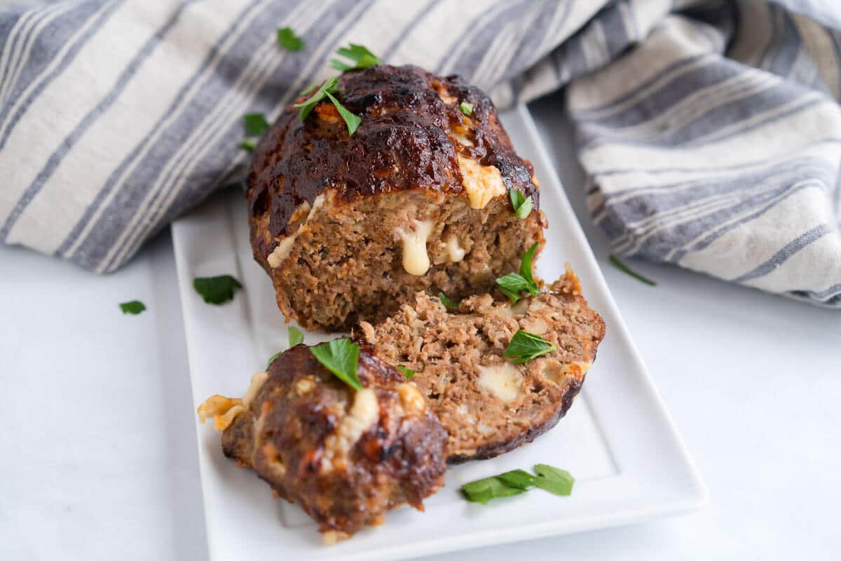 Front view of sliced meatloaf with cheese dripping from the front.