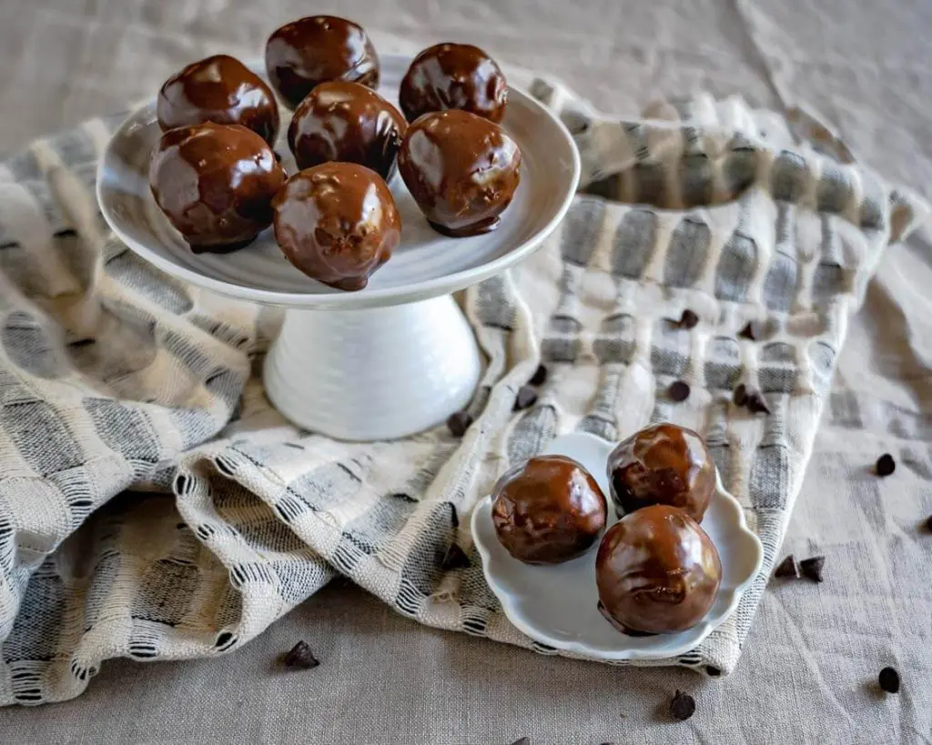 Side view of a stack of chocolate balls sitting on a white cake stand over a blue and white napkin with chocolate chips scattered.