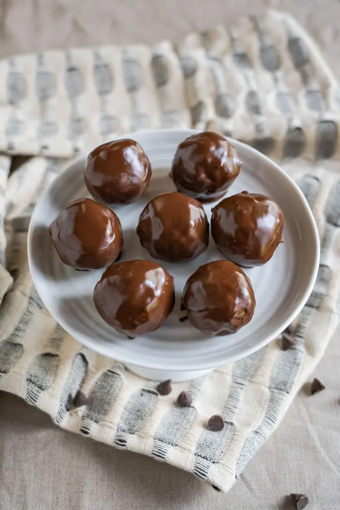 Top down view of chocolate peanut butter balls on a white cake stand over a blue and white napkin scattered with chocolate chips.