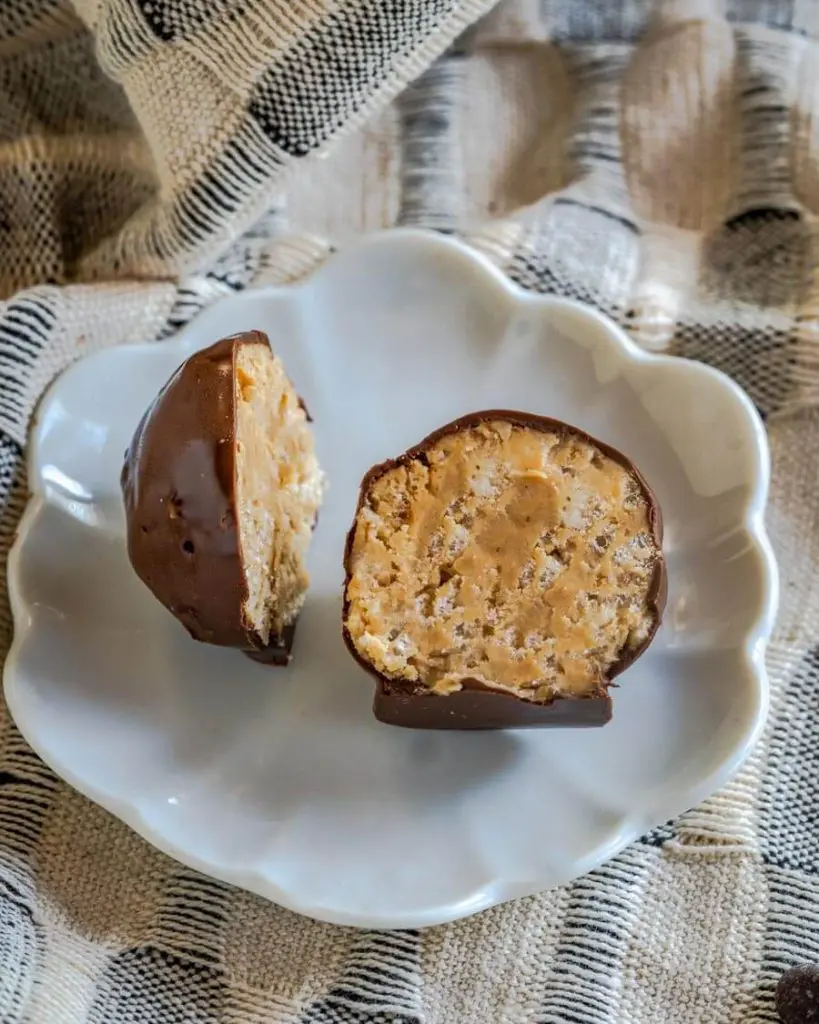 A chocolate peanut butter ball cut in half sitting on a white plate over a blue and white napkin.