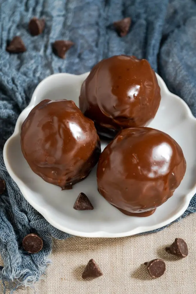 Top down view of three chocolate covered balls on a white plate with chocolate chips scattered around it.