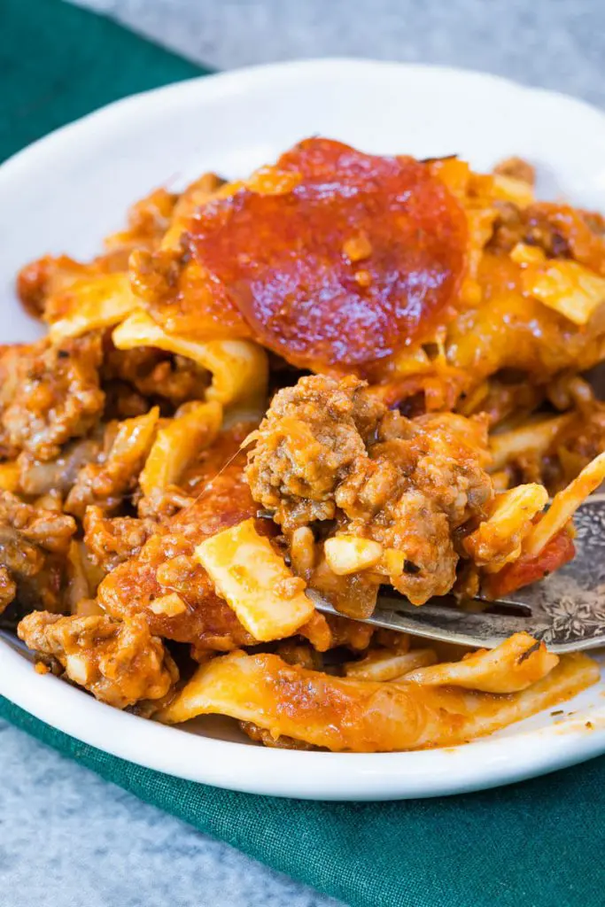 Cheese casserole filled with beef and noodles and topped with pepperoni on a white plate over a green napkin.