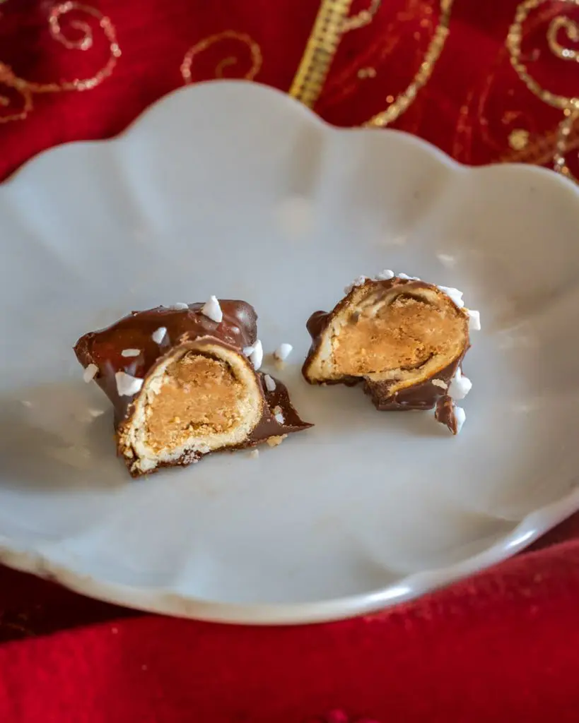 A chocolate covered pretzel bite cut in half sitting on a white plate over a red napkin.