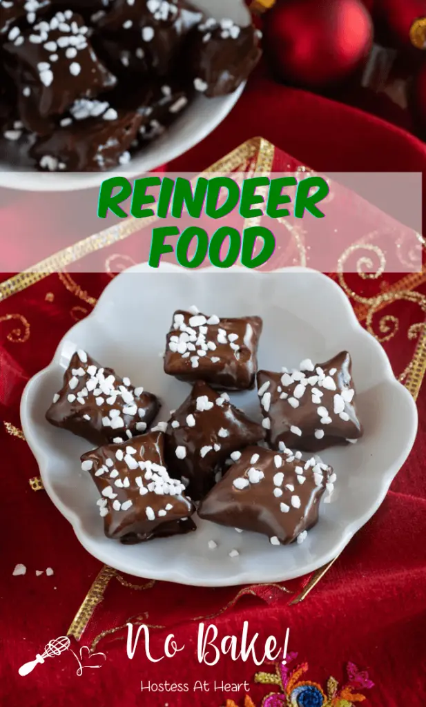 Top down view of chocolate covered Reindeer Food Recipe using pretzel bites garnished with pearl sugar sitting on a white plate over a red napkin net to Christmas bulbs. A second plate sits in the background.