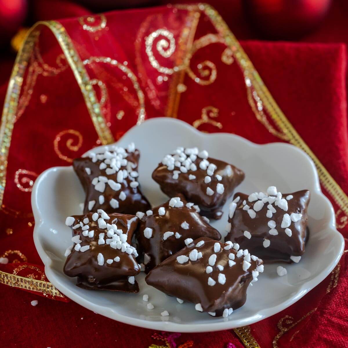 Close up sideview of chocolate covered pretzels bites topped with Swedish Pearl Sugar sitting on a white plate.