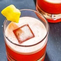 Top down view of a rocks glass filled with a red foam-topped Campari Cocktail garnished with a piece of pineapple.