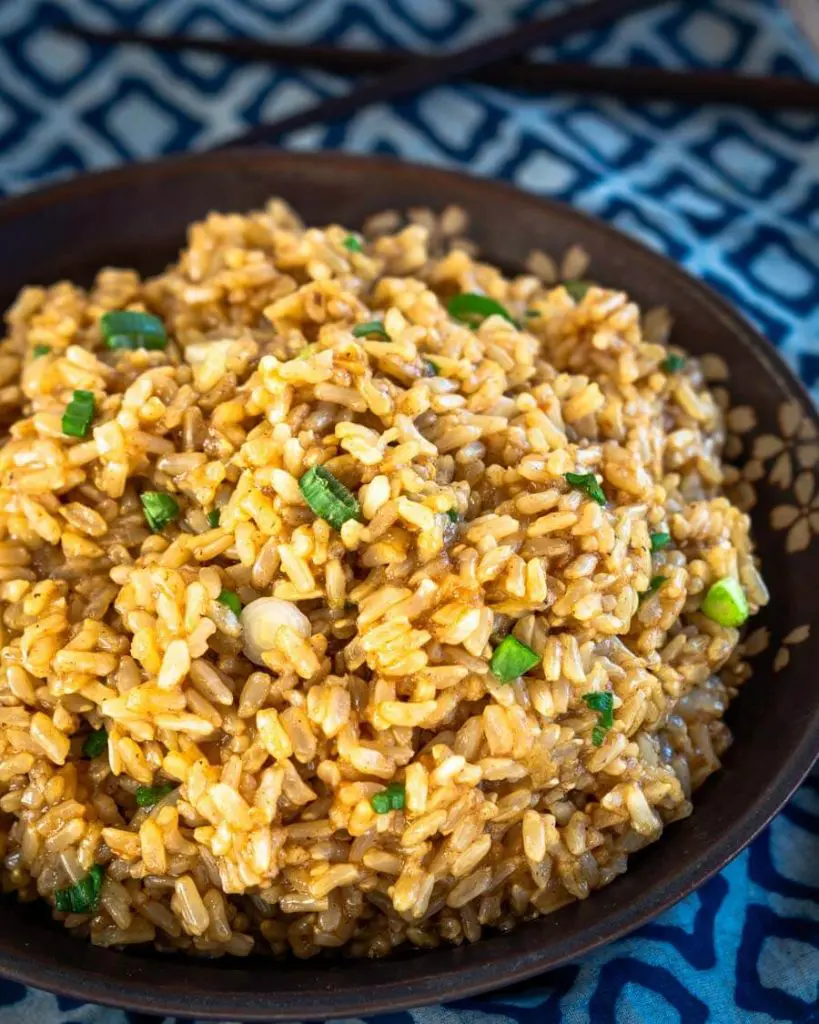 Top down view of a bowl filled with saucy brown rice garnished with sliced green onion.