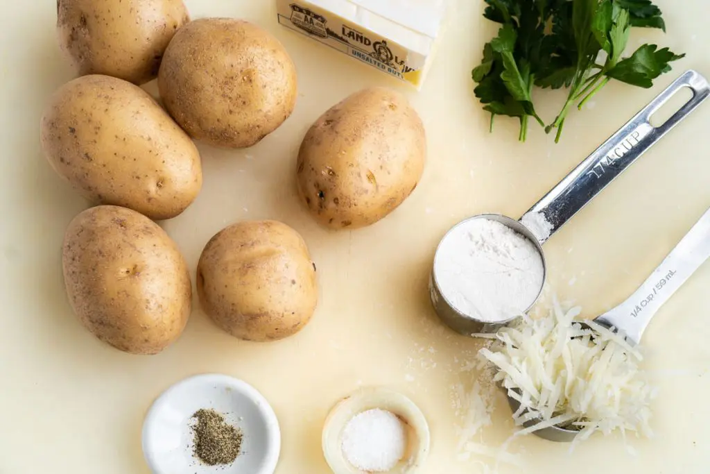 A cutting board holding potatoes, flour, parmesan, butter, parsley, salt and pepper