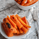 Side view of roasted sliced carrots in a white dish. A second dish sits in the background.