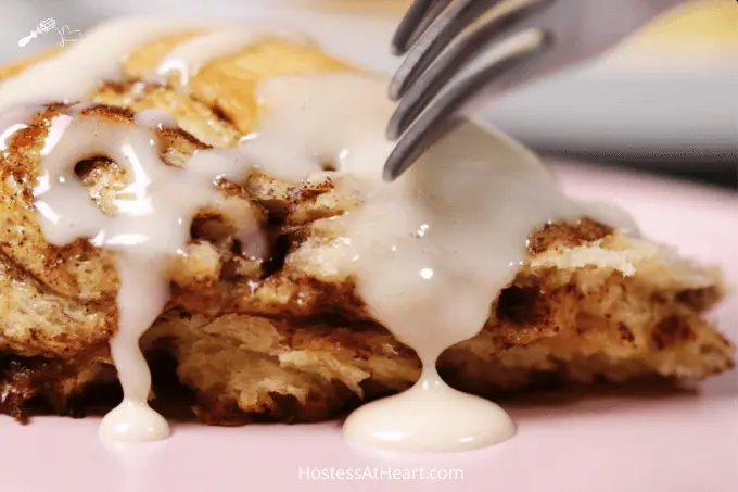 Close up side shot of a cinnamon roll with glaze dripping down the side and a fork about to cut into it.