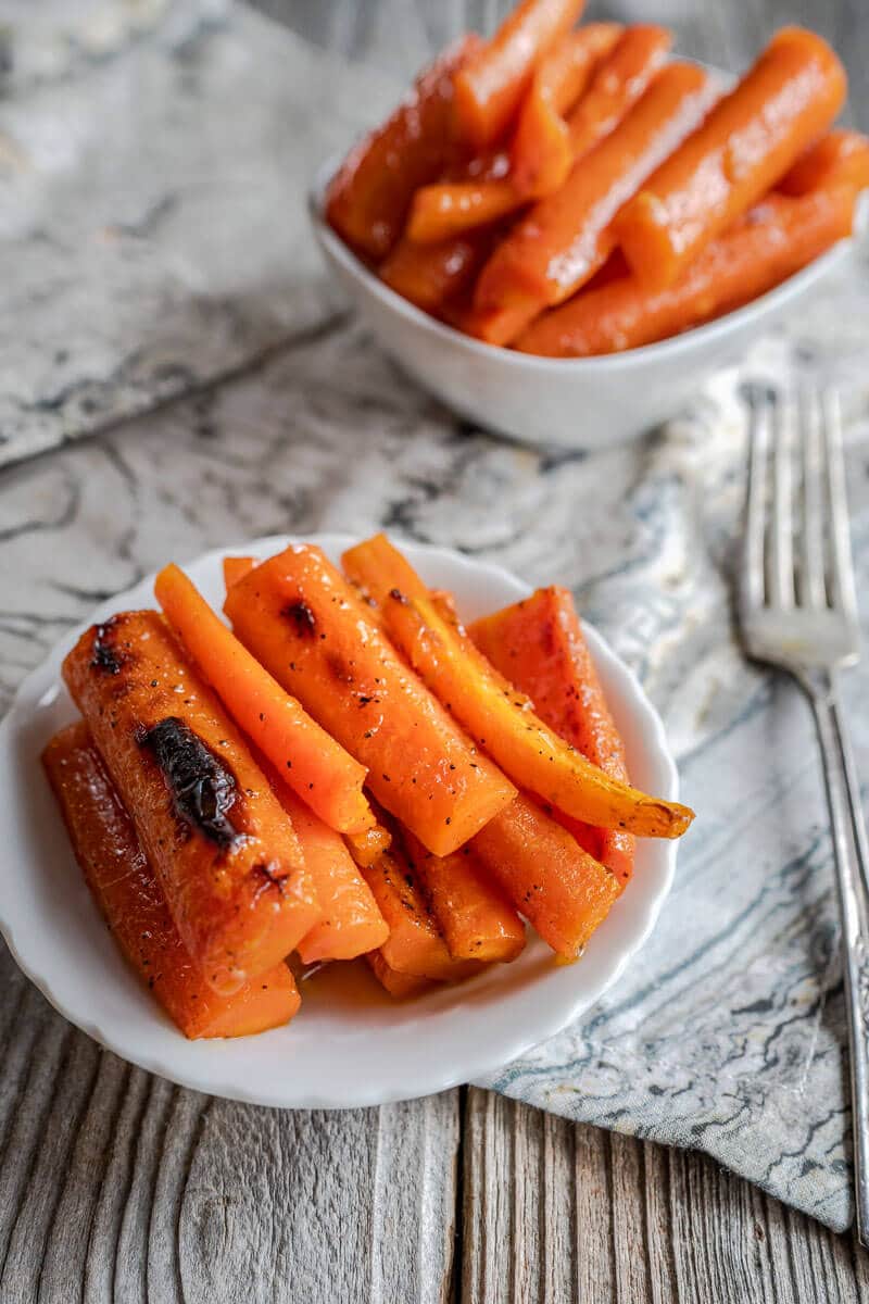 Top down photo of roasted carrot sticks in a white dish with a second dish in the background.