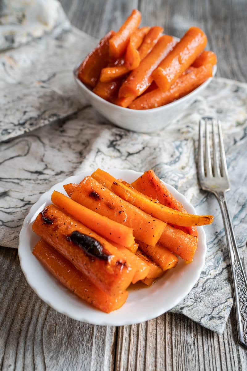 Slices of oven roasted carrots in a white dish. A second dish sits in the background.