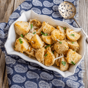 Closeup angle view of crispy parmesan crusted potatoes in a baking dish with a serving spoon sitting to the back.