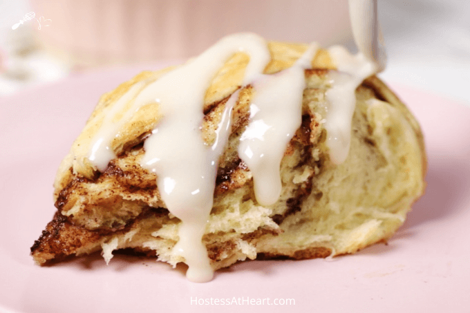 Side view of a slice of a cinnamon roll with glaze being poured over it.