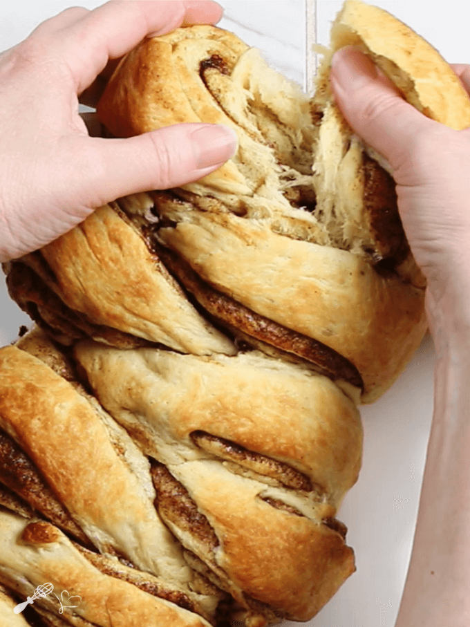 Two hands tearing a loaf of cinnamon brioche pull-apart roll apart showing how soft and tender it is.