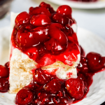 3/4 angle of a slice of meringue dessert topped with a cherry raspberry filing.