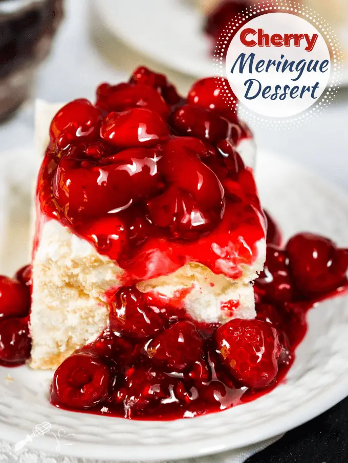 Table view of a white plate holding a piece of meringue dessert topped with a cherry raspberry sauce.