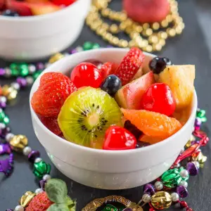 A white bowl filled with chunks of fresh fruit and surrounded by colorful beads.