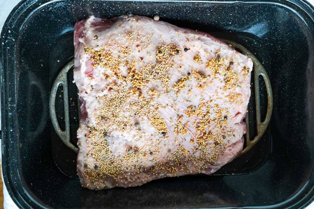Uncooked corned beef brisket sitting on grates inside a roasting pan.