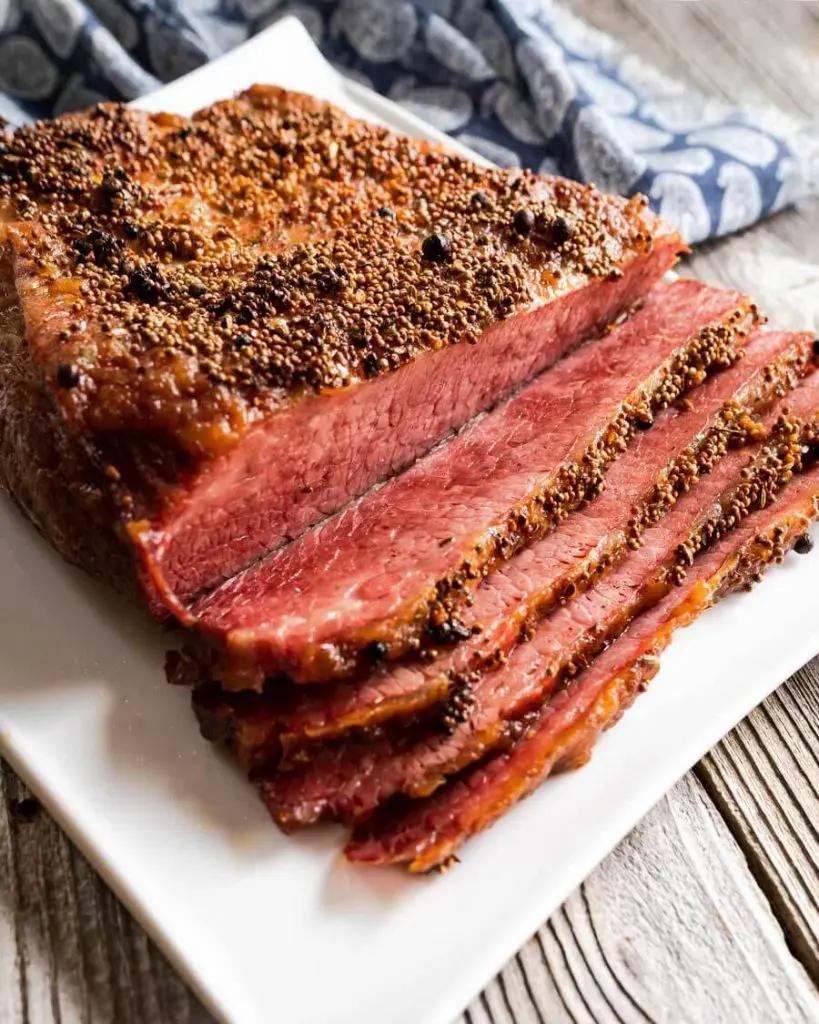3/4 side view of a baked corned beef brisket that's been sliced and sitting on a white platter.