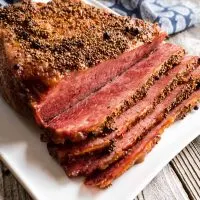 Top down of a baked and sliced corned beef brisket sitting on a white plate.