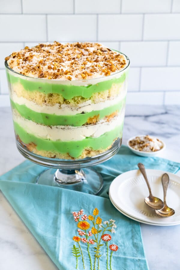 Side view of a trifle bowl containing layers of cake, pudding, whipped topping and garnished with a mixture of toasted coconut and pecans.