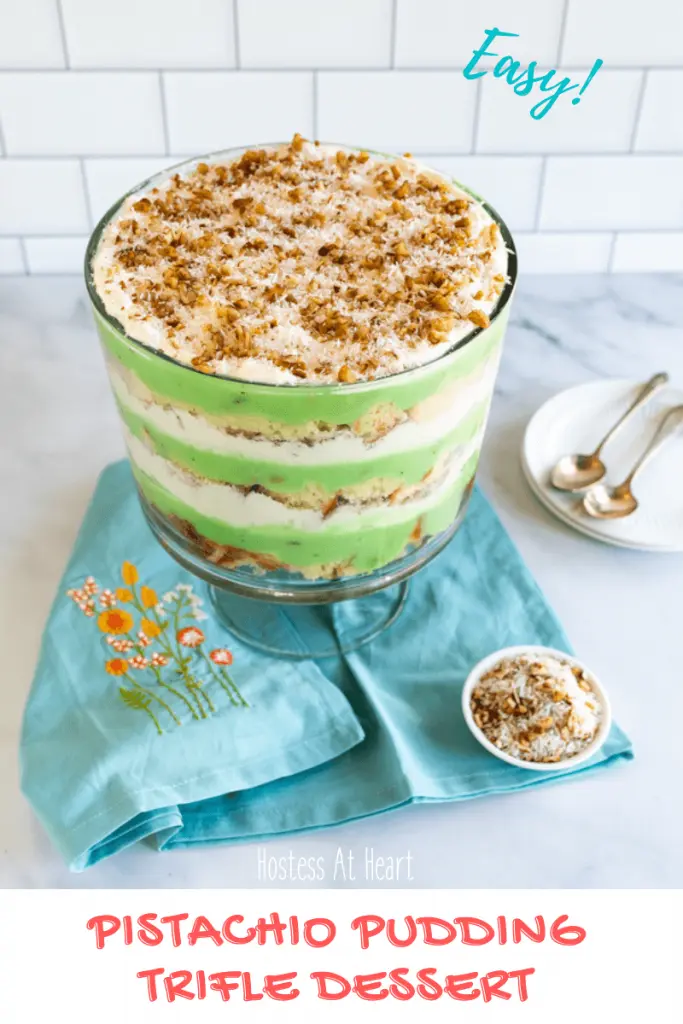 3/4 angle photo of a trifle bowl filled with pistachio pudding, cake, whipped cream and topped with toasted coconut with pecans.