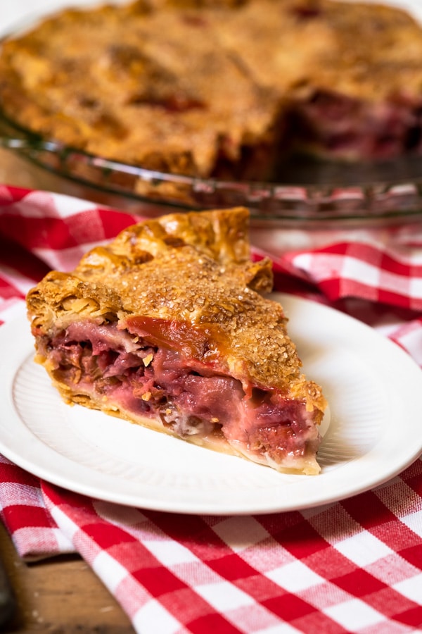 A slice of old-fashioned strawberry rhubarb pie on a plate in front of a whole pie. 